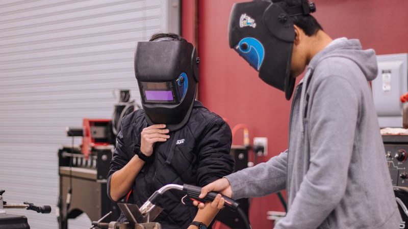 An apprentice welding under supervision in a college workshop